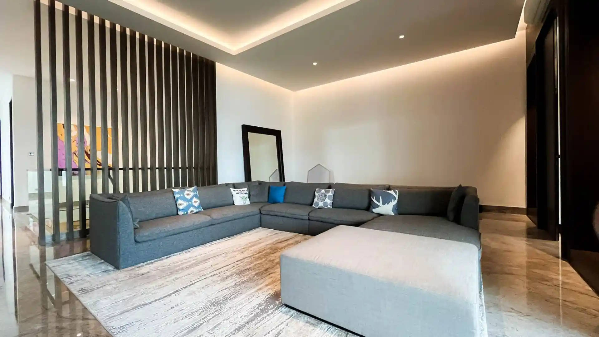 Interior ruang tamu mewah dengan sofa L, partisi kayu, dan pencahayaan hangat